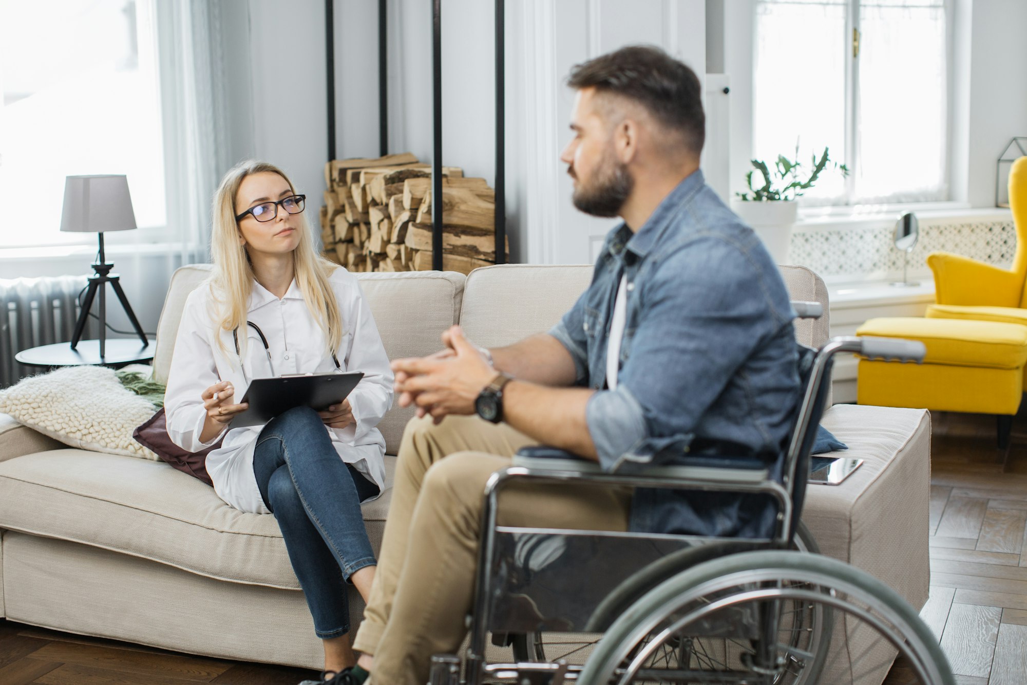 Female doctor consulting disabled man at living room